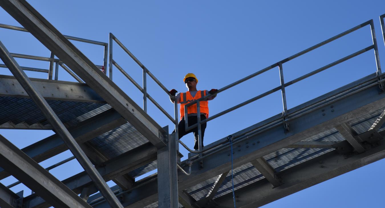 Construction worker standing on steel walkway against blue sky