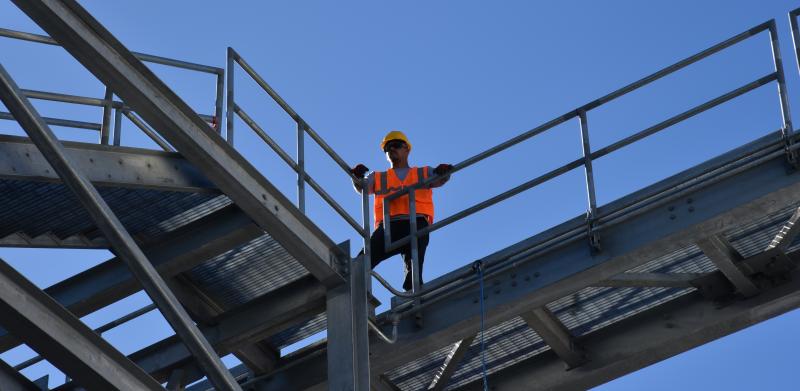 Construction worker standing on steel walkway against blue sky